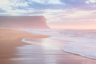 Sunrise ignites the sky in pink hues beside the cliff face at Garie Beach in a vibrant beach landscape. Pink wall art.
