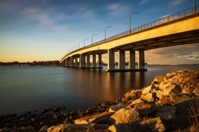 Sunset casting a golden glow on the Captain Cook Bridge, mirrored in the Georges River for striking nature art.
