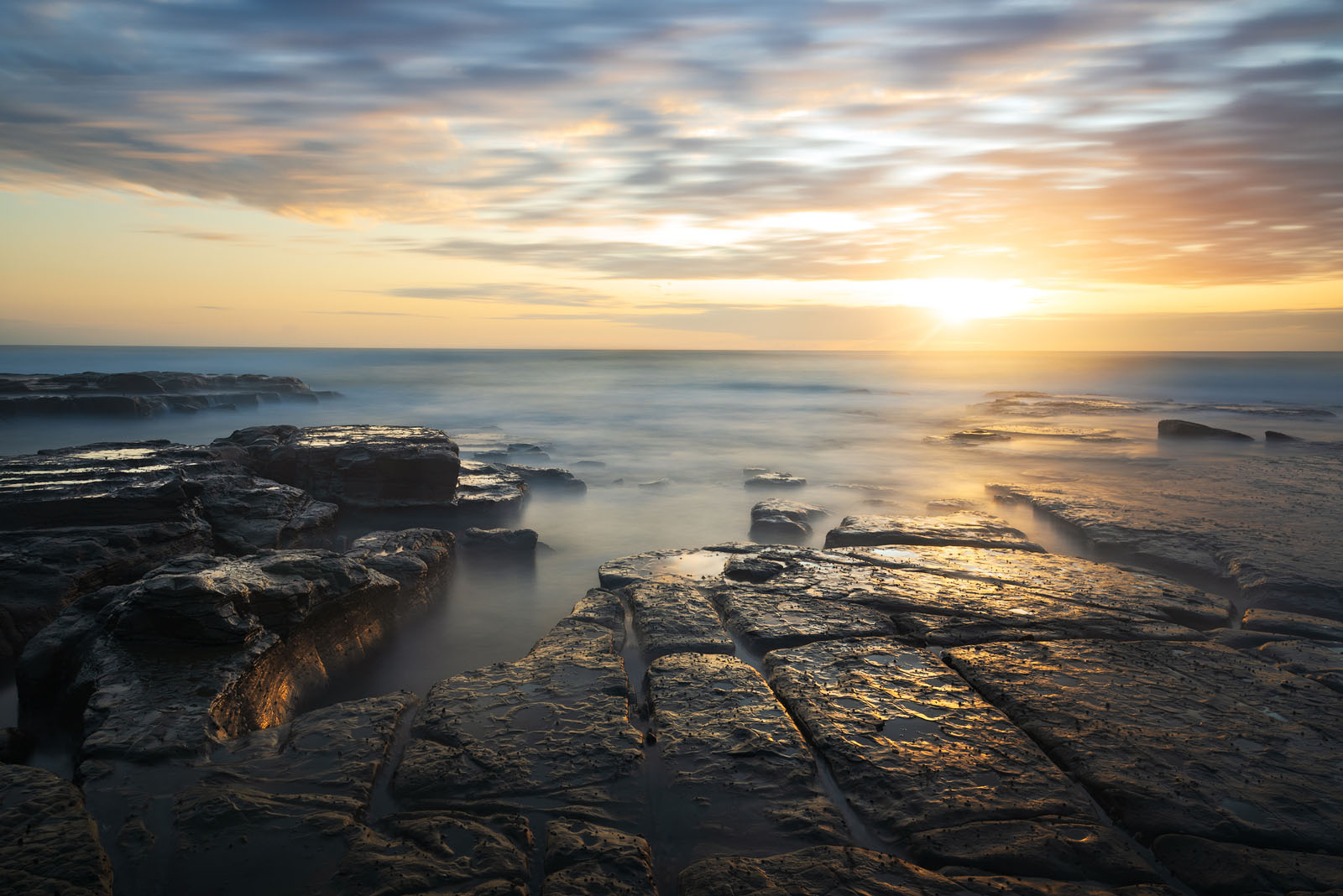 Golden sunrise over the textured rocks and calm sea at Bulgo Beach.