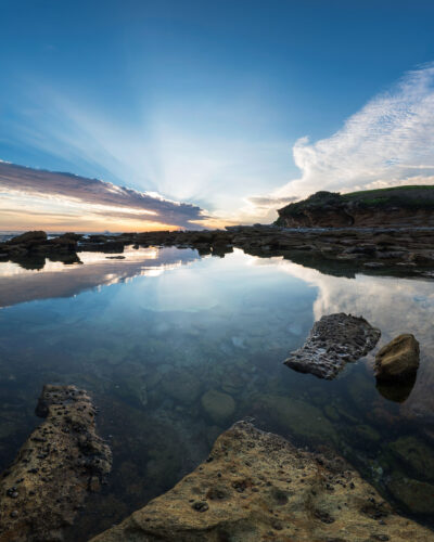 Dawn at Little Bay Beach with a serene sky reflected in the calm waters, captured as beach wall art.