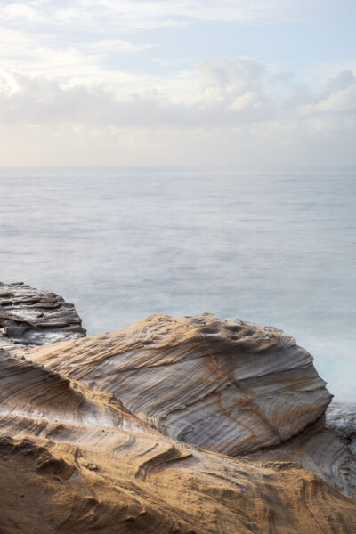 Textured sandstone meets calm seas at Mahon Pool, a serene coastal scene in subtle natural hues.
