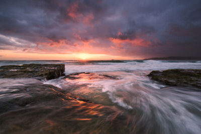 Dynamic waves crash under a fiery sunrise at Maroubra Beach, showcasing the natural energy of the ocean in this coastal scene.