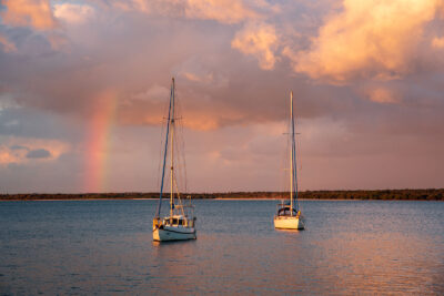 A subtle rainbow arcs over sailboats at Taren Point during sunset in this enchanting nature art piece.