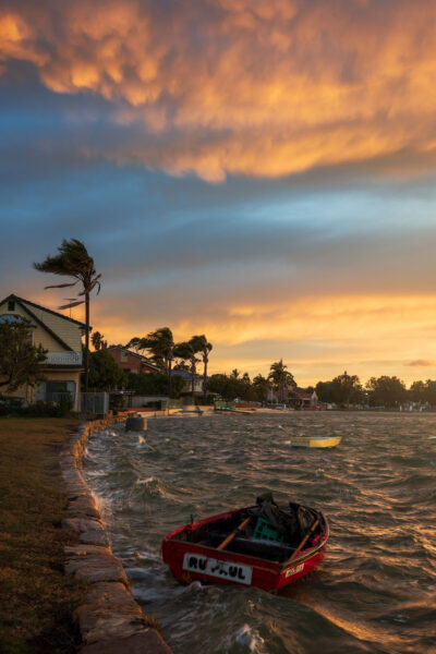 A boat rocking on the waves at Taren Point under a sunset sky's fiery dance, captured in vibrant landscape art.
